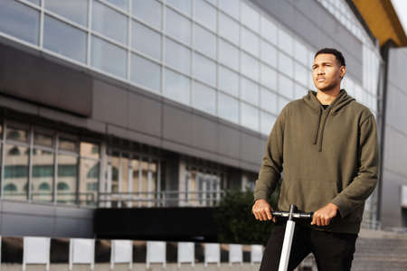 young african american man in casual clothing posing on electric scooterの写真素材