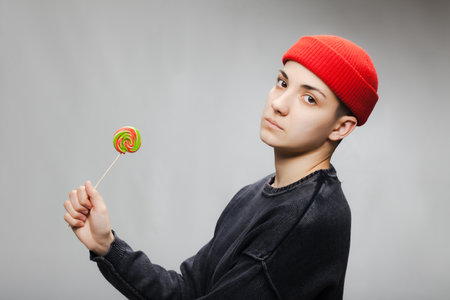 Girl with short hair and a lollipop wearing blouse and red hat against gray background.の写真素材