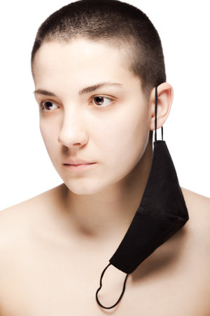 Cute girl with very short hair wearing black protective face mask hanging on her ear. Studio...
