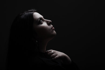 Side lit silhouette portrait of a girl looking up against black backgroundの写真素材