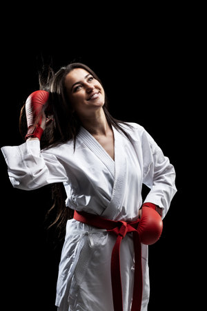 beautiful happy girl girl posing and smiling in karate outfit kimono and red gloves against black backgroundの写真素材