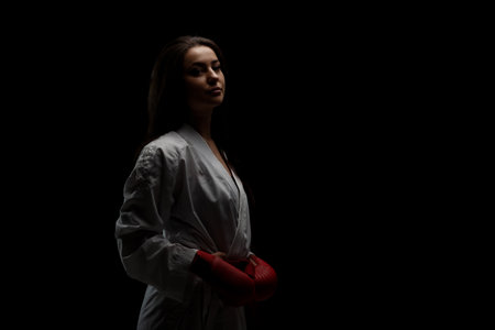 beautiful girl posing in karate outfit kimono and red gloves against black backgroundの写真素材