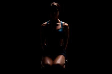 Female runner backlit abstract silhouette. Girl in sportswear posing against dark background.の写真素材