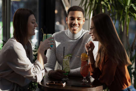 Three multiracial friends in a bar cheering. After work party with cocktails after successful work day.の写真素材
