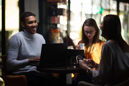 Three multiracial business colleagues having a meeting after work or during coffee break in a restaurant. Friends working at a cafe bar.の写真素材