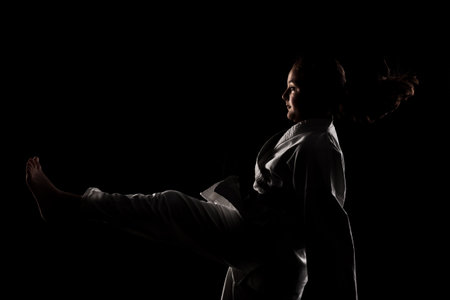 Young girl exercising karate. Child in kimono against black background.の写真素材