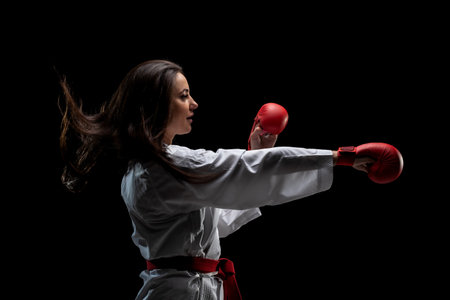 girl exercising karate punch wearing kimono and red gloves against black backgroundの写真素材