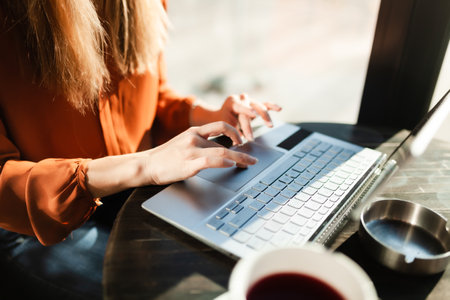 Young businesswoman in a cafe bar or restaurant with bright sunlight. Freelancer girl working on laptop and having tea at a window table. Abstract photo.の写真素材