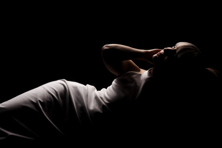 Beautiful girl with blond bangs fringe wearing white fashionable fancy dress lying against black background.の写真素材