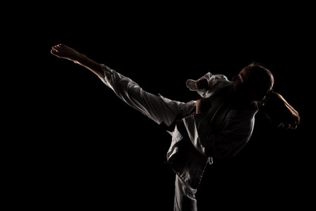 Young girl exercising karate. Child in kimono against black background.の写真素材