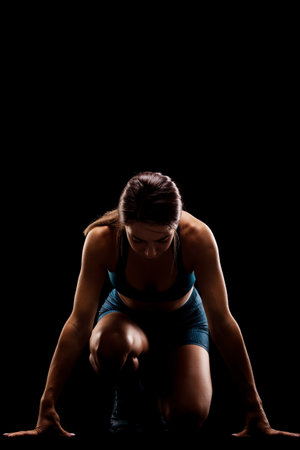 Female runner in low race start position. Girl in sportswear against dark background.の写真素材