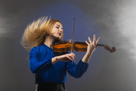 Beautiful blond girl playing violin. Female violinist doing energetic movement with hair in the air...