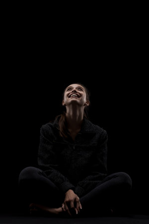 cute caucasian girl relaxing after yoga exercise against dark backgroung. side lit looking up and smilingの写真素材
