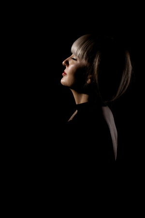 Beautiful girl with blond bangs fringe against black background. Abstract sidelit portrait.の写真素材