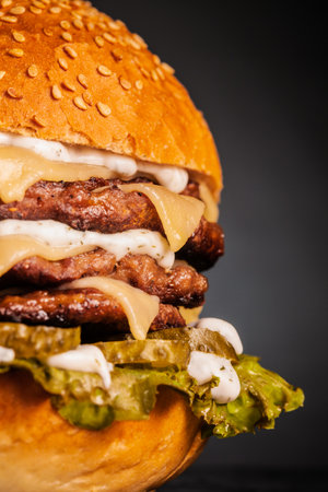 Abstract fast food. Quadruple burger with cheese cucumber and lettuce. Junk food against dark background.の写真素材
