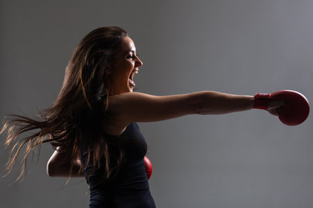 beautiful girl exercising karate punch and screaming  with hair in the air against gray backgroundの写真素材