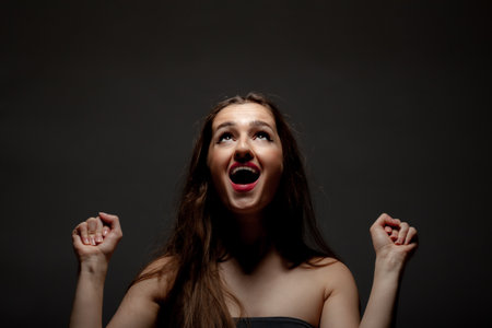 Beautiful girl studio portrait. Making hand and face gestures against dark background.の写真素材