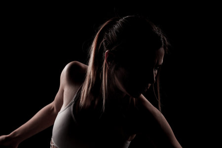 Beautiful caucasian girl posing yoga in shadow. side lit photo on black background.