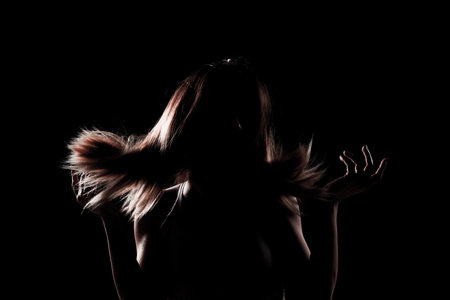 silhouette contour of a beautiful girl with blowing hair. Side lit studio portrait on dark...