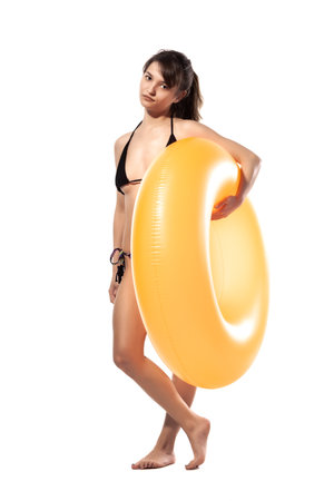 Beautiful young sexy woman in black swimsuit holding orange inflatable rubber ring isolated on white background. Summer pool sea resort concept.の写真素材