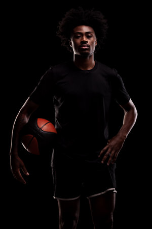 Basketball player holding a ball. Young african american sports man against black background.の写真素材