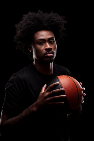 Basketball player holding a ball against black background. Serious concentrated african american man.の写真素材