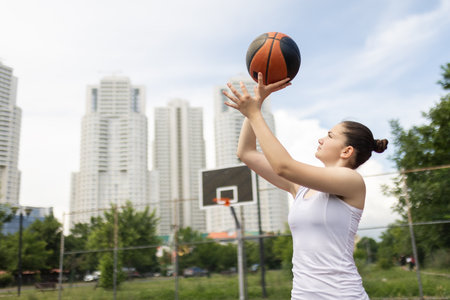Young girl playing basketball. Holding ball in hands. Outdoor sports field with urban background.