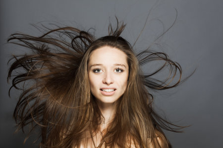 brunette girl with flowing hair in the air studio portrait against gray background.の写真素材