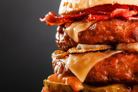Abstract double burger with bacon cheese onions tomatoes cucumber. Against dark background.の写真素材