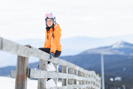 Beautiful skier girl posing sitting on a wooden fence.の写真素材