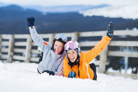 Skier friends posing lying on the snow. Two beautiful ski girls outdoors.の写真素材
