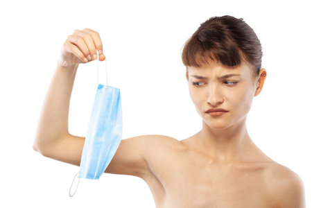 Portait of a beautiful girl holding medical face mask against viruses pollution or dust. Angry face and hand gesturesの写真素材