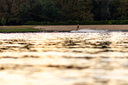 Female wakeboarder wakesurfing on sunset. Girl riding waterski cabel. Holding tow rope. Summer activities in the lake.の写真素材