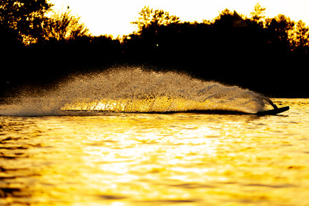 Silhouette of a wakeboarder wakesurfing on sunset. Throwing water in the air.の写真素材
