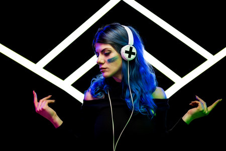 A woman with vibrant blue hair wearing headphones against abstract light shape made of white neon ledの写真素材