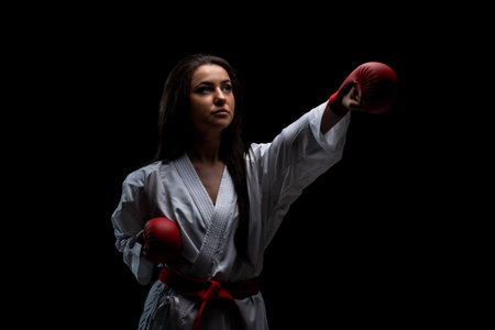 girl exercising karate punch wearing kimono and red gloves against black backgroundの写真素材