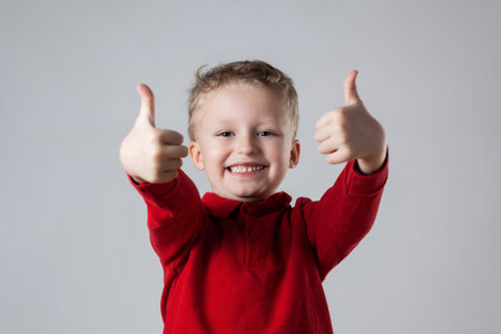 A young boy wearing a red shirt is smiling and giving a thumbs up gestureの写真素材