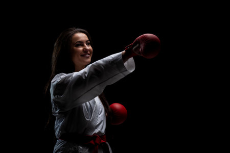 karate girl smiling in kimono and red gloves against black background