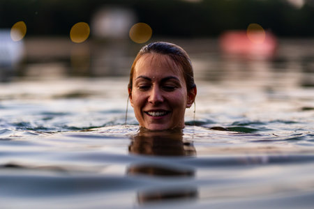 Smiling woman enjoying a peaceful swim in a tranquil lake at sunsetの写真素材
