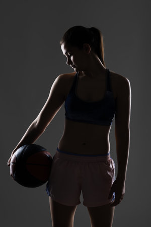 A silhouette in a sports outfit holds a basketball. The image captures their contours and athletic physique.の写真素材