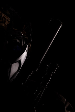 A dark minimalist image showcasing a masked figure with advanced technology accessories and weapons. The dim lighting adds intrigue and mystery, suggesting themes of science fiction, security, and anonymity.の写真素材