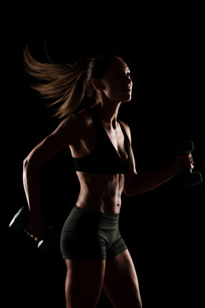 Strength and fitness depiction of a woman performing exercises with dumbbells. Features an intense atmosphere and highlights the dedication to workout and personal training.の写真素材