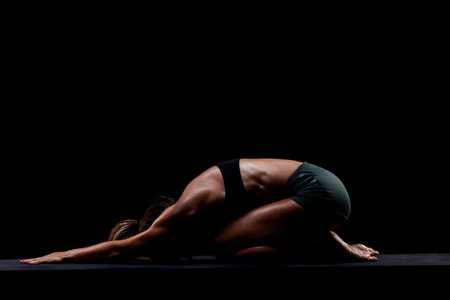 Person performing a yoga pose emphasizing strength, flexibility, and balance. Photographed in a dimly lit setting highlighting muscle definition and focus in fitness.の写真素材