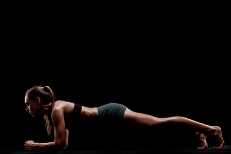 Fitness display of a woman engaging in a plank pose. Black backdrop emphasizes her athleticism and dedication to exercise and physical wellness.の写真素材