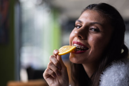 Smiling woman with dental braces enjoying a slice of lemon while seated indoors