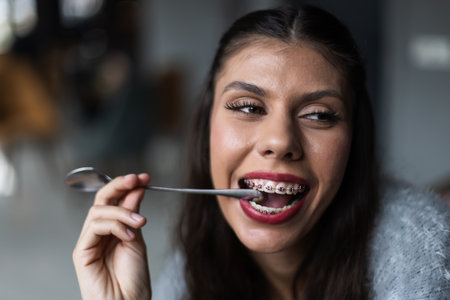 Smiling young woman enjoying a relaxing moment while playfully holding a spoon showing dental braces