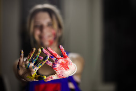 Joyful female artist with a blurred background presenting her hands splattered with vibrant paint colors, expressing artistic creativity.の写真素材