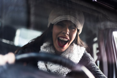 Frustrated woman sitting in car wearing winter clothing and expressing emotions while gripping the...