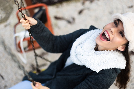 Smiling young woman with braces enjoying a swing outdoors during autumnの写真素材