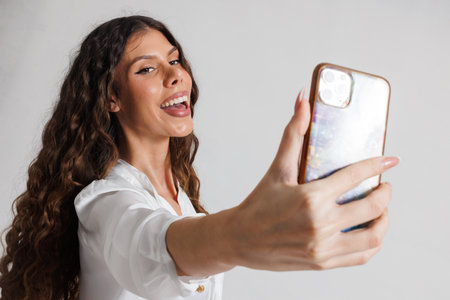 Woman Taking a Selfie Smiling Happily in a Casual Setting Using Her Smartphoneの写真素材
